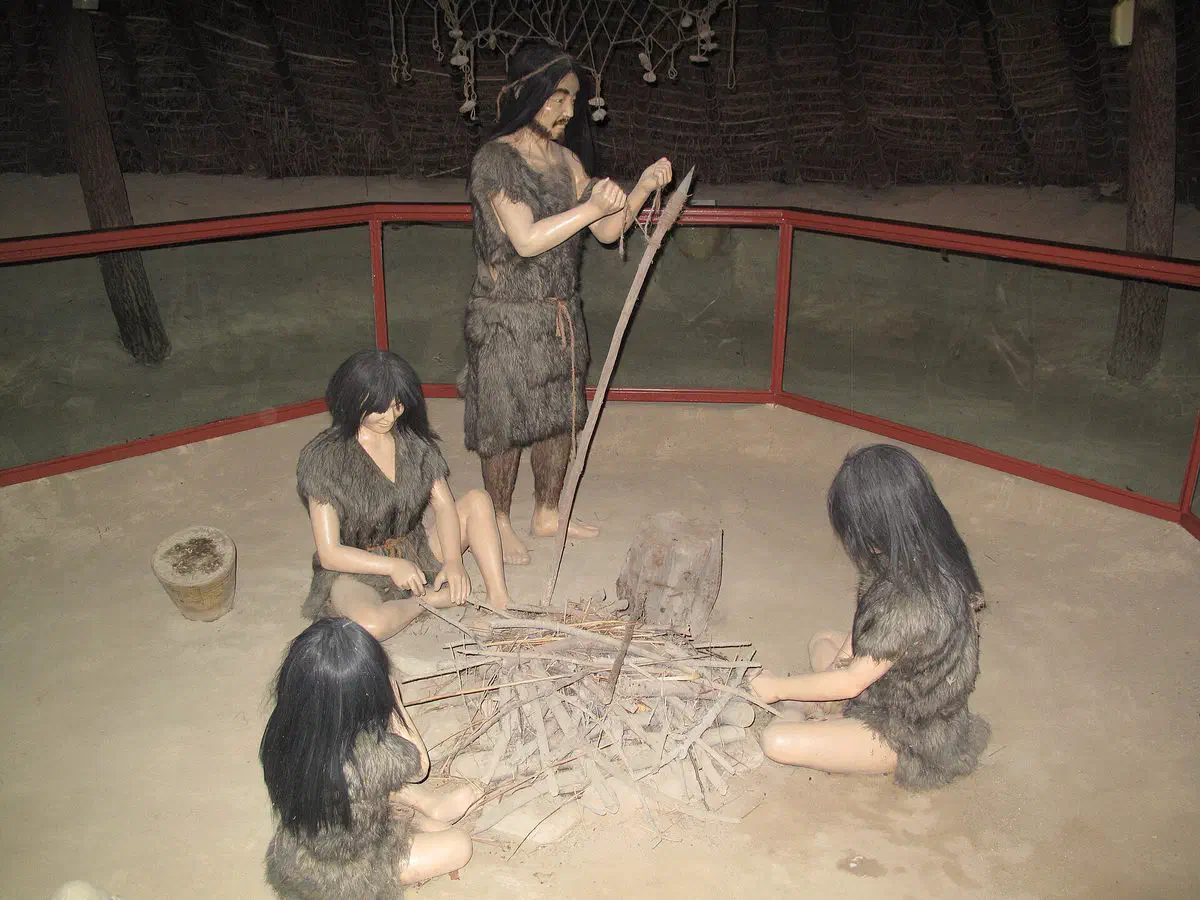 A mannequin diorama inside a reconstructed pit-house at Amsa-dong, showing a Neolithic family in fur clothing working around a fire pit