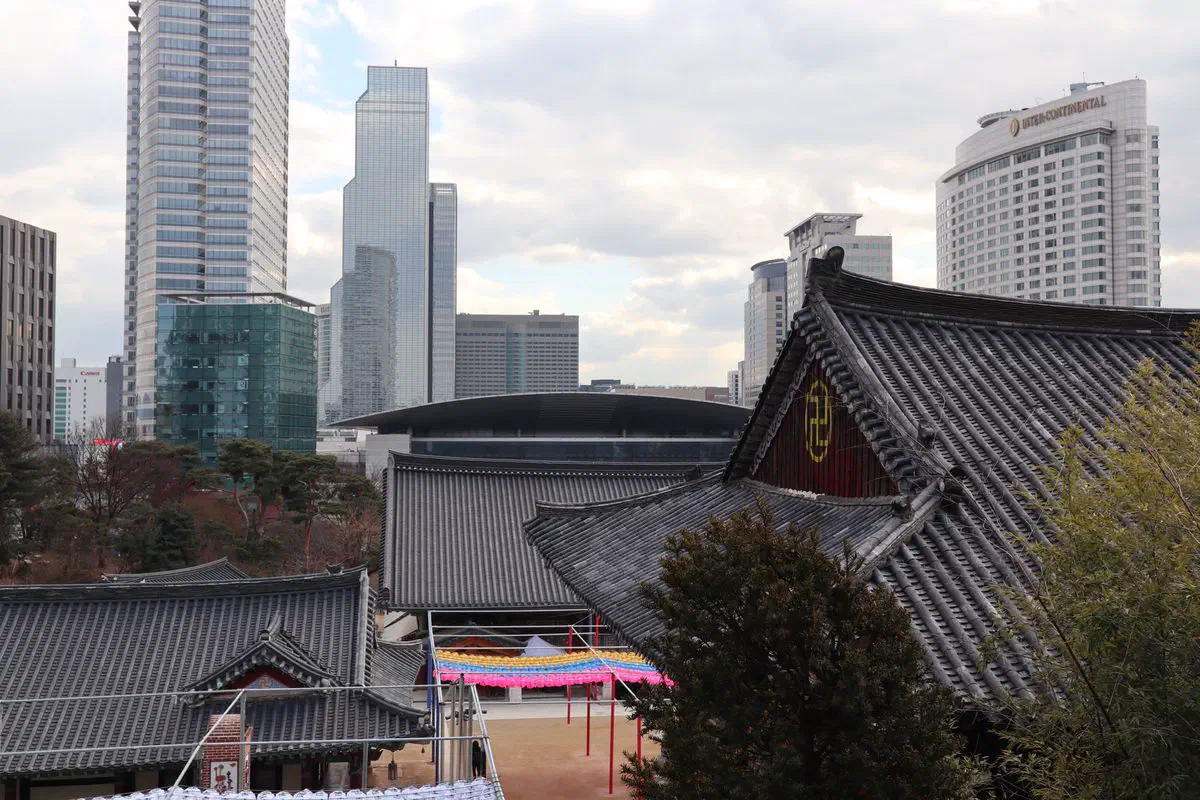 Bongeunsa temple's traditional tiled roofs in the foreground, with Samseong-dong's skyscrapers — including COEX and the InterContinental Hotel — rising directly behind