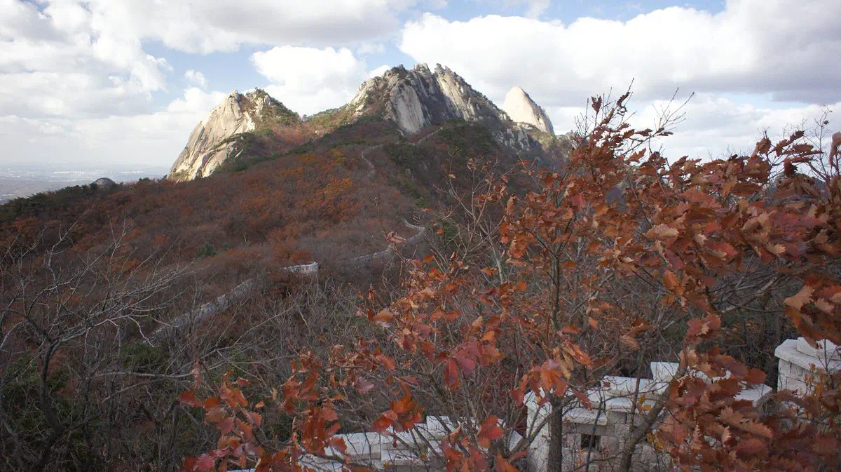 A restored section of the Bukhansanseong fortress wall running along Bukhansan's ridge in autumn foliage
