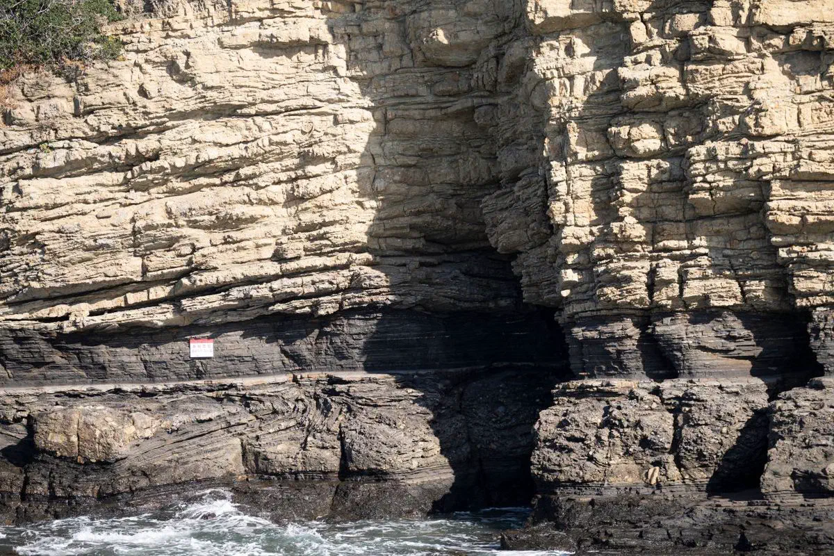 Chaeseokgang's stratified sedimentary cliff, layers of rock stacked like books above a sea cave carved by the tide