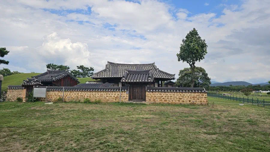 A tile-roofed gatehouse and stone wall beside one of the tomb mounds at Daereungwon