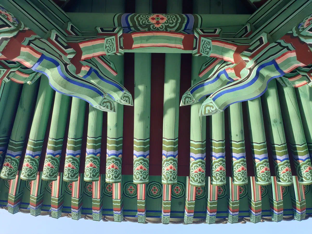 Rows of painted rafter ends radiating out from a pavilion's eaves at Deoksugung's Daehanmun gate, Seoul, blue sky beneath