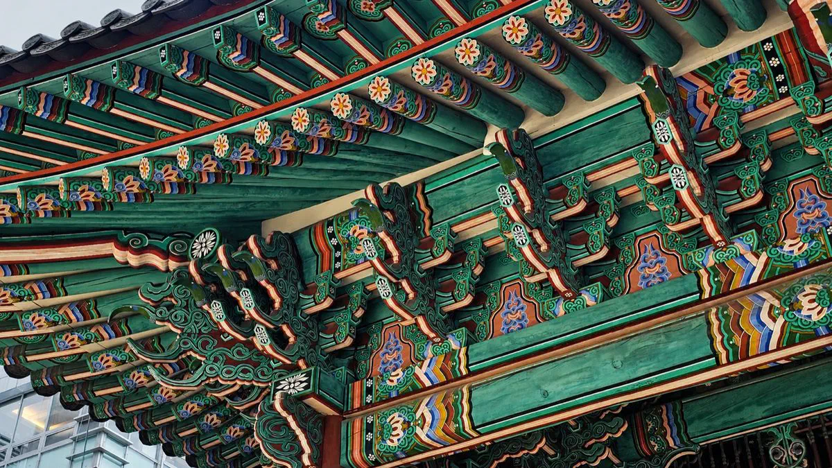 Close detail of dancheong paintwork under the eaves at Deoksugung's Daehwamun gate, showing the layered five-color bracket pattern