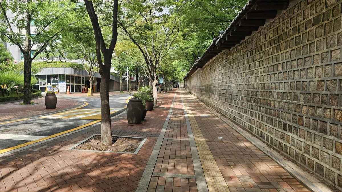 A brick walking path running alongside Deoksugung's stone wall, lined with trees and large earthenware pots