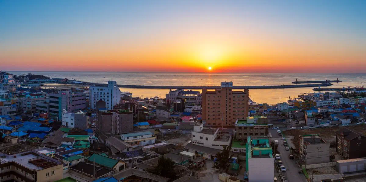 Jumunjin harbor at sunrise, its breakwater and lighthouses visible where it meets the open sea — the setting for Goblin's best-known scene