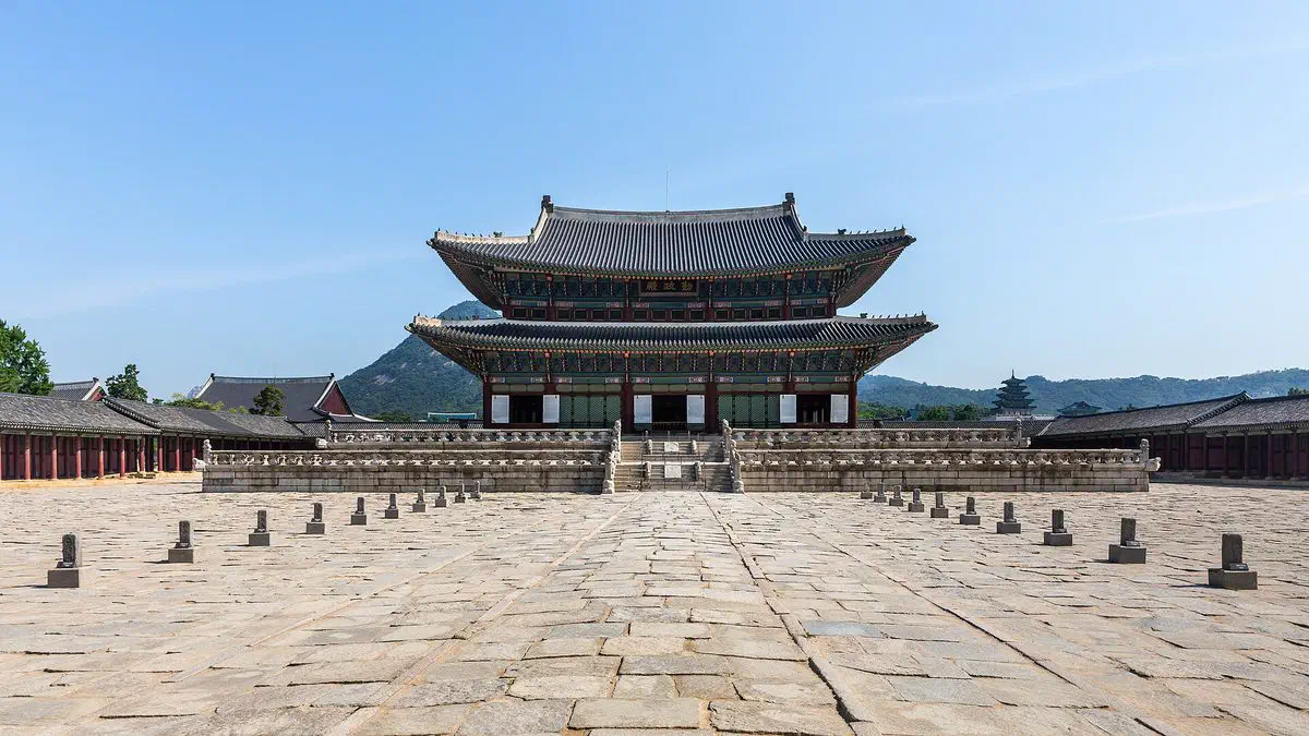 The front facade of Geunjeongjeon, Gyeongbokgung's throne hall, its double-tiered roof and courtyard stairs in full view under a clear sky