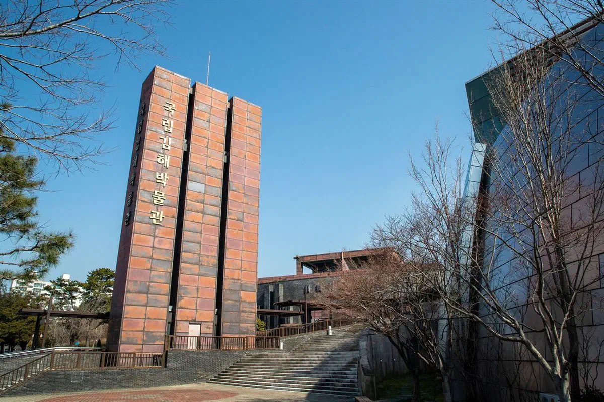 Gimhae National Museum's entrance tower, clad in rust-coloured oxidised metal with the museum name running vertically down it, and the dark brick museum buildings behind