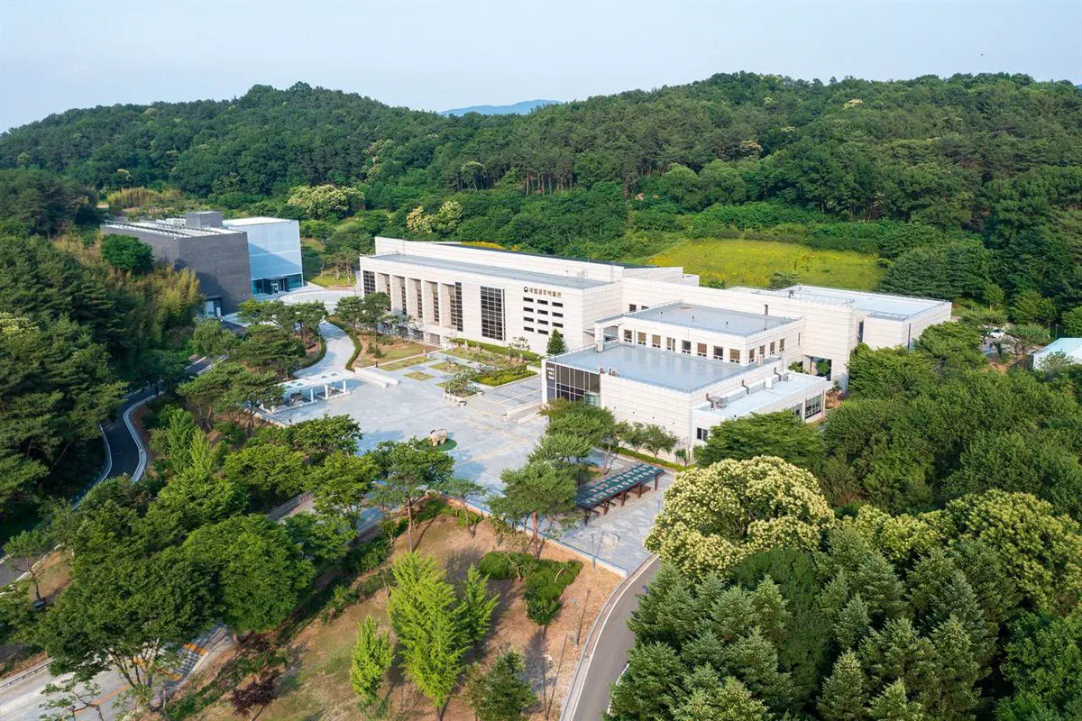 Aerial view of Gongju National Museum: pale stone buildings with a colonnaded front, a paved forecourt, and wooded hills closing in behind