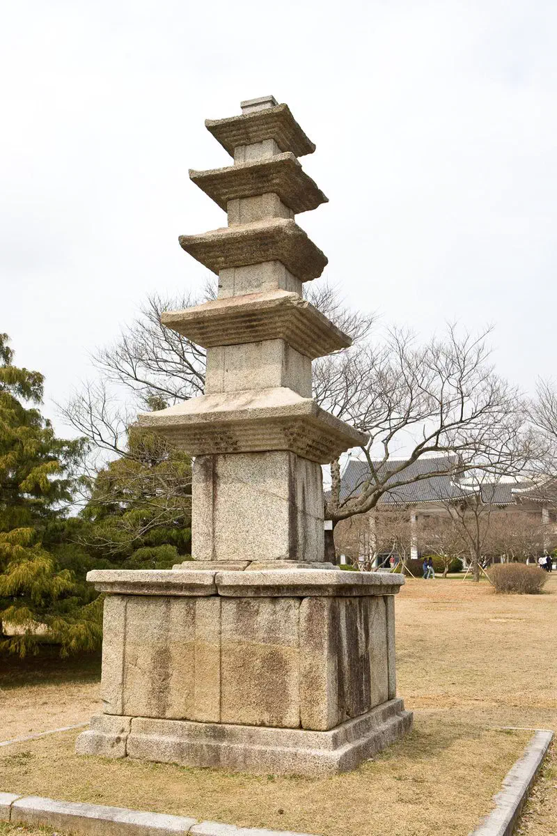 A five-story stone pagoda standing on the open grounds of Gwangju National Museum in winter, with the museum's tiled roof among bare trees behind it