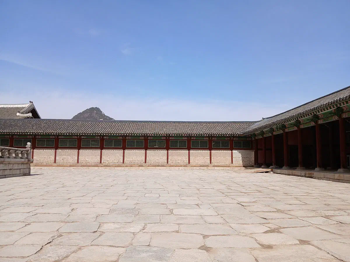 A stone courtyard inside Gyeongbokgung palace, corridor buildings on both sides and Bugaksan mountain rising behind the walls