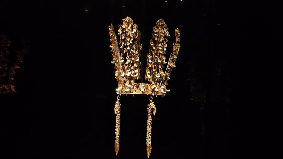 A Silla gold crown with jade curved-bead ornaments and dangling pendants, lit against a black background at the National Gyeongju Museum