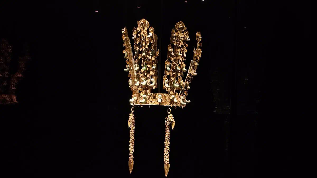 A Silla gold crown with jade curved-bead ornaments and dangling pendants, lit against a black background at the National Gyeongju Museum