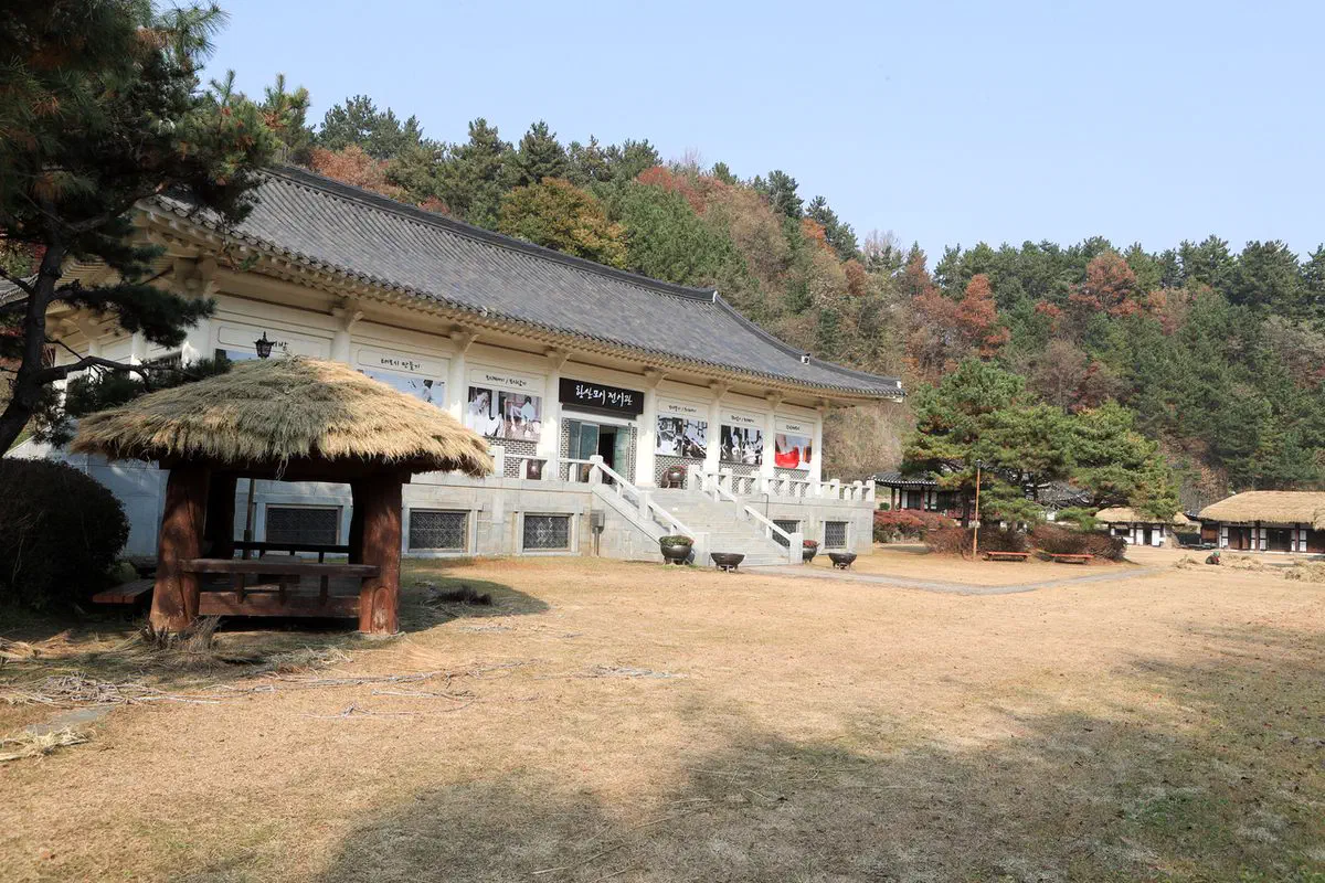 The Hansan Mosi Museum's exhibition hall in Seocheon, a hanok-style building with a thatched rest pavilion in front, surrounded by autumn trees