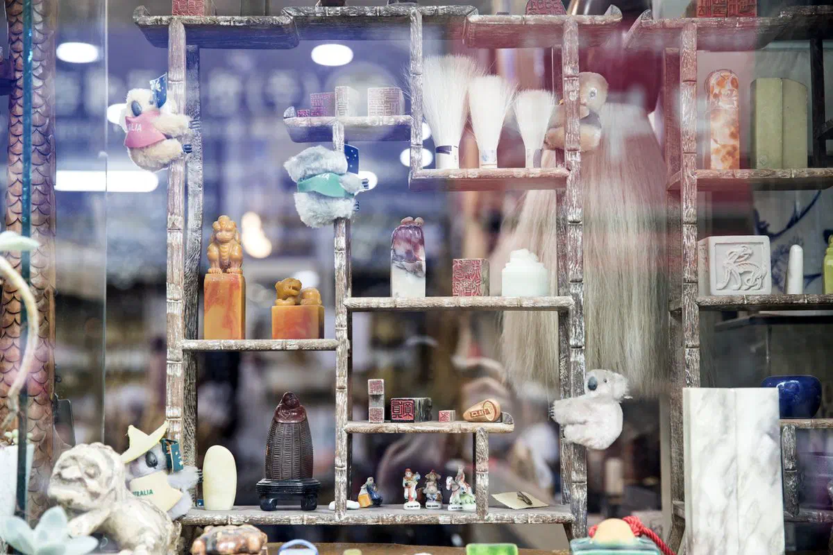An Insadong shop window: carved stone name seals with lion finials, calligraphy brushes and small figurines arranged on wooden shelves, with souvenir koala plush toys among them