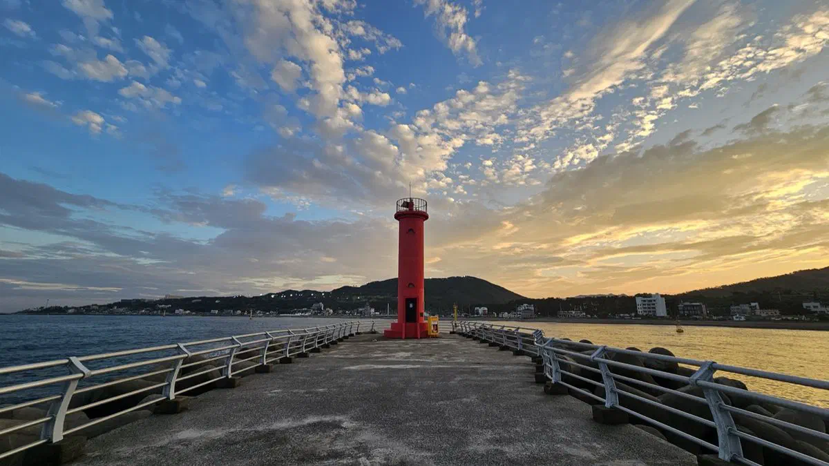 A red lighthouse at the end of Jeonchon Harbor's breakwater, lit by the last light of sunset