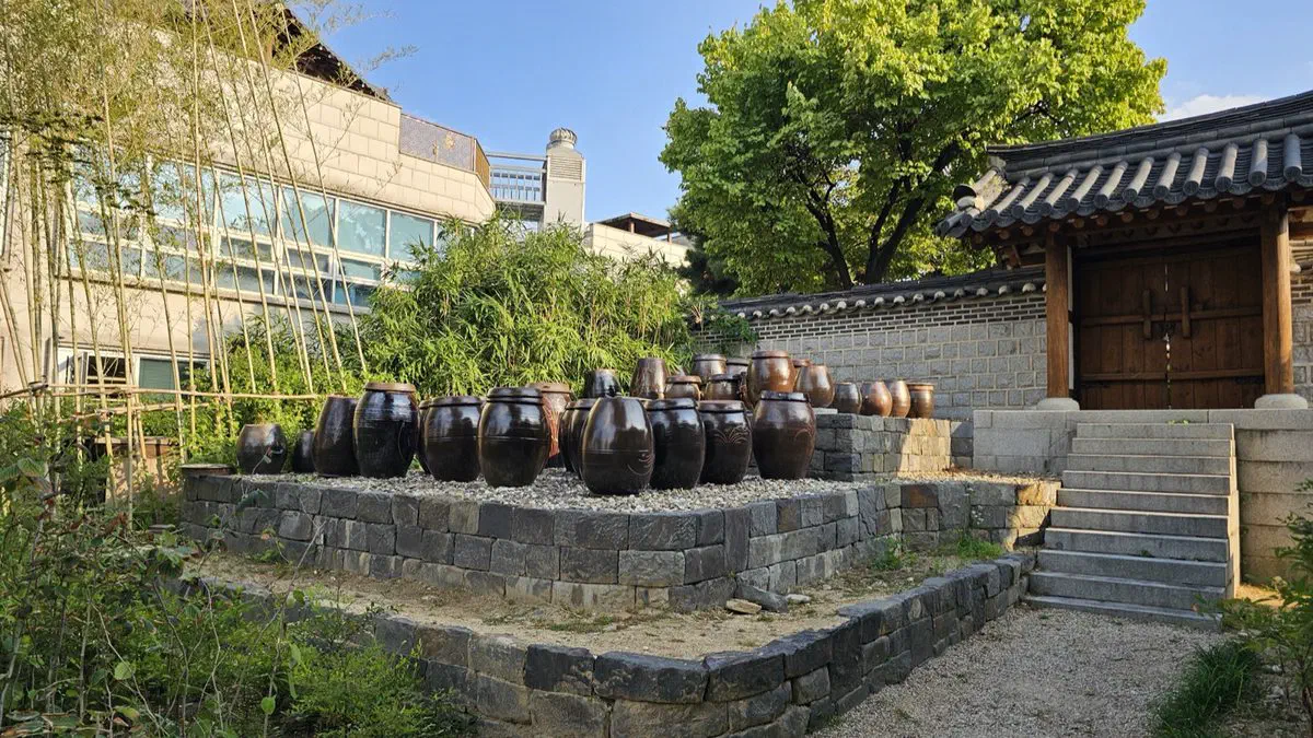 Dark clay jars set out on a stone terrace beside a wooden gate and bamboo