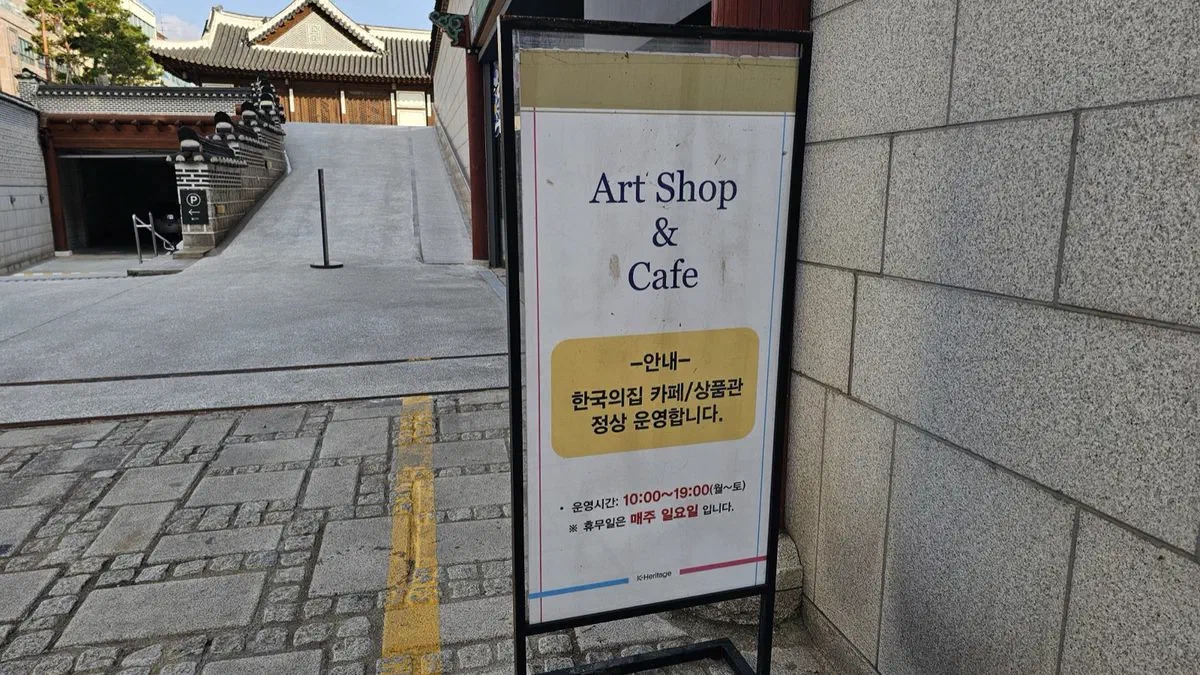 Sandwich-board sign for the Korea House Art Shop and Cafe giving hours 10:00 to 19:00, Monday to Saturday, closed Sundays