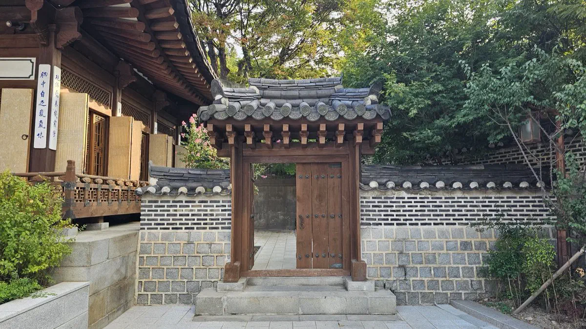 A small tile-roofed wooden gate in a grey brick wall at Korea House