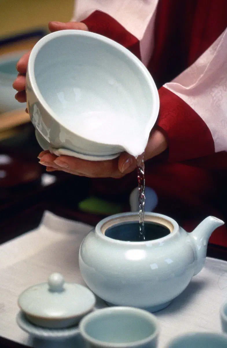 A tea ceremony in hanbok, water poured from a celadon bowl into a teapot before steeping