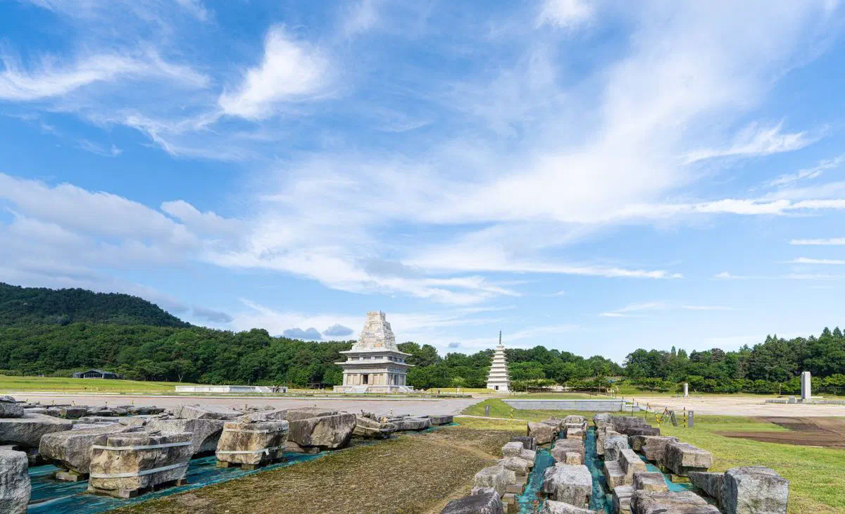 The Mireuksa temple site with both pagodas visible: on the left the west pagoda, rebuilt only to the height that survived and stopping in a ragged break, and on the right the east pagoda reconstructed as a complete nine-story tower, with the exposed foundation stones of the vanished temple in the foreground