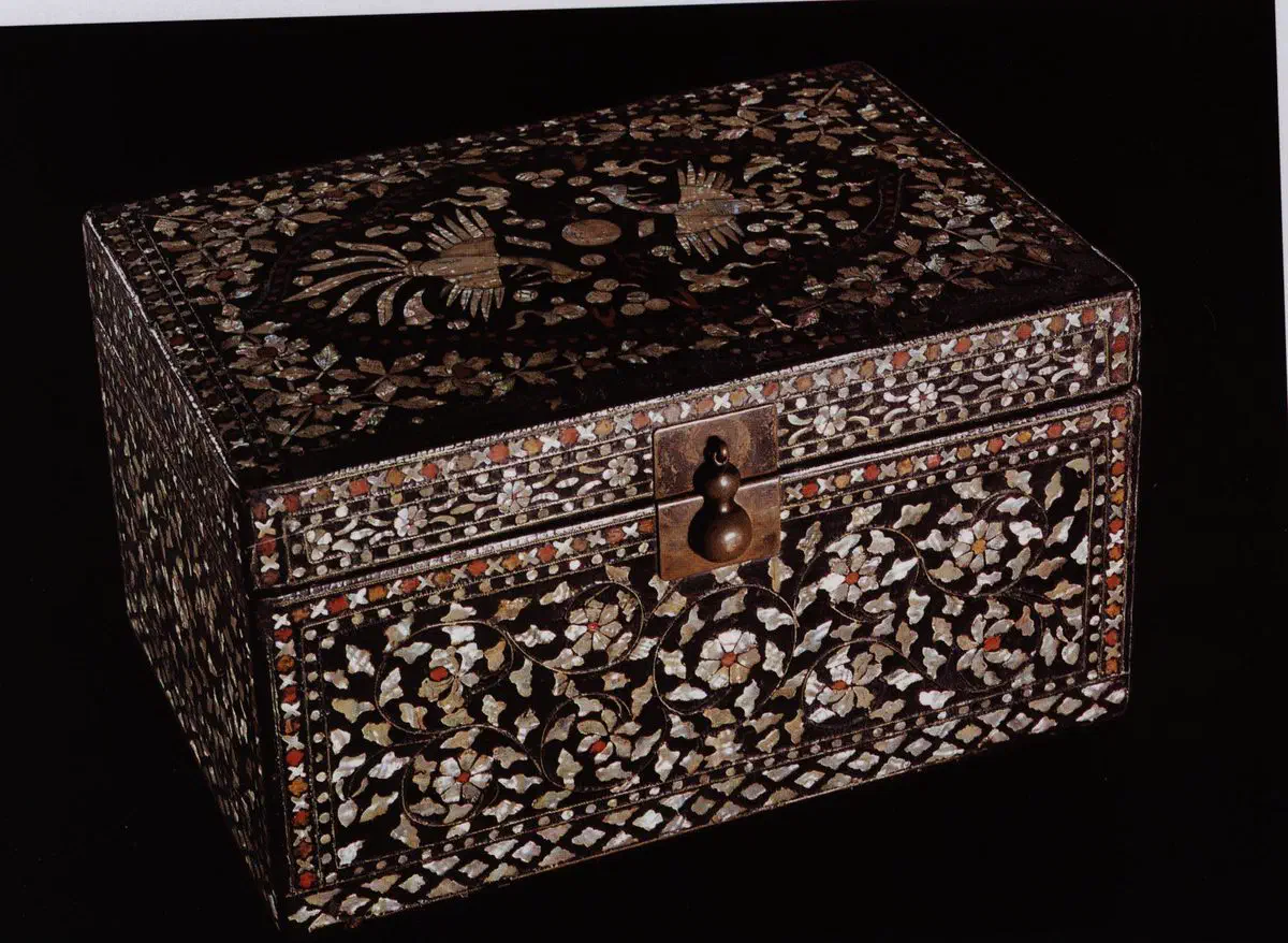 A Korean wedding box in black lacquer, its lid inlaid with a pair of birds among flowering scrolls in mother-of-pearl, with reddish amber-toned pieces set among the white shell and a brass gourd-shaped clasp