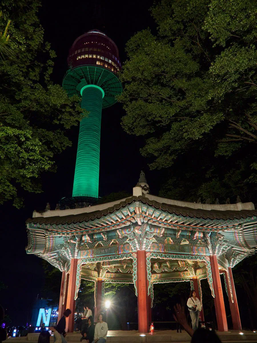 N Seoul Tower illuminated at night, seen behind a traditional Korean pavilion on Namsan