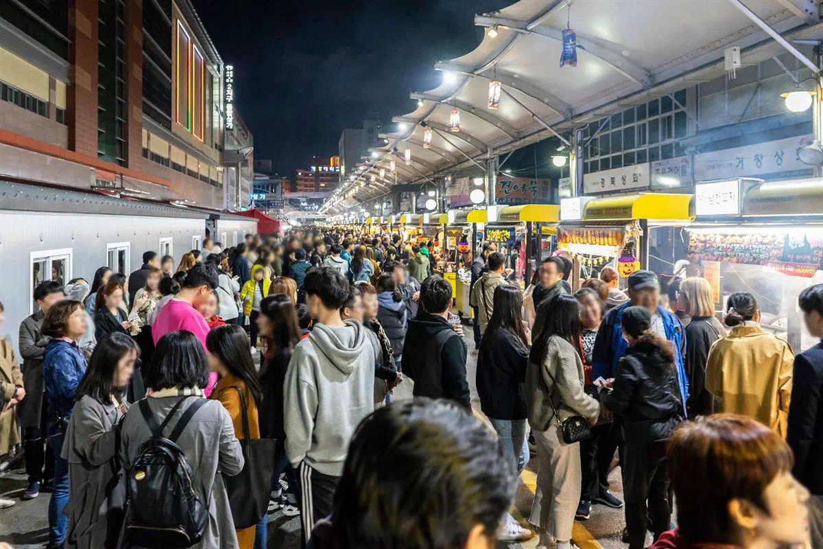 Seomun Market at night in Daegu, packed with people between rows of lit food stalls under a white canopy, with shop signs glowing above the crowd