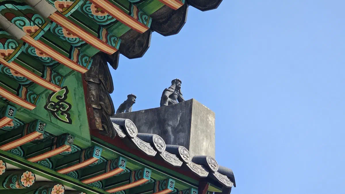 Small stone figures on the ridge end of a ritual hall roof, above green and red dancheong brackets
