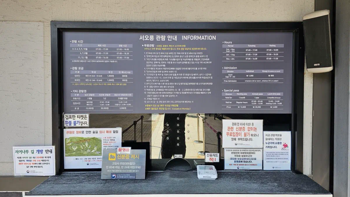 Ticket booth at Seooreung with a bilingual board of hours, admission fees and special passes, and notices posted around it