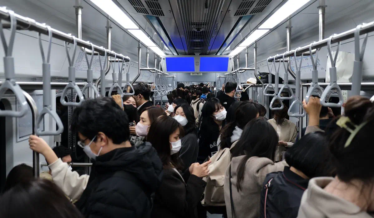 A packed Seoul subway car during rush hour, passengers standing shoulder to shoulder holding the overhead straps