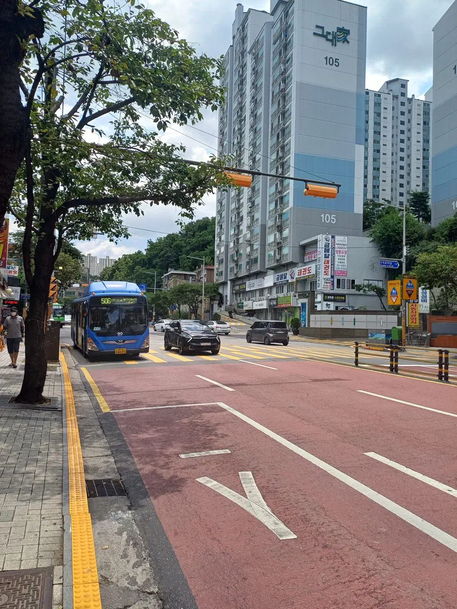 A blue trunk-line city bus, route 506, approaching a stop in a dedicated red bus lane in Seoul