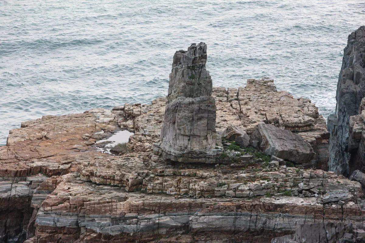 A tall standalone rock pillar at Taejongdae's Sinseondae cliff, Busan, standing on the edge of a sheer coastal rock platform above the sea
